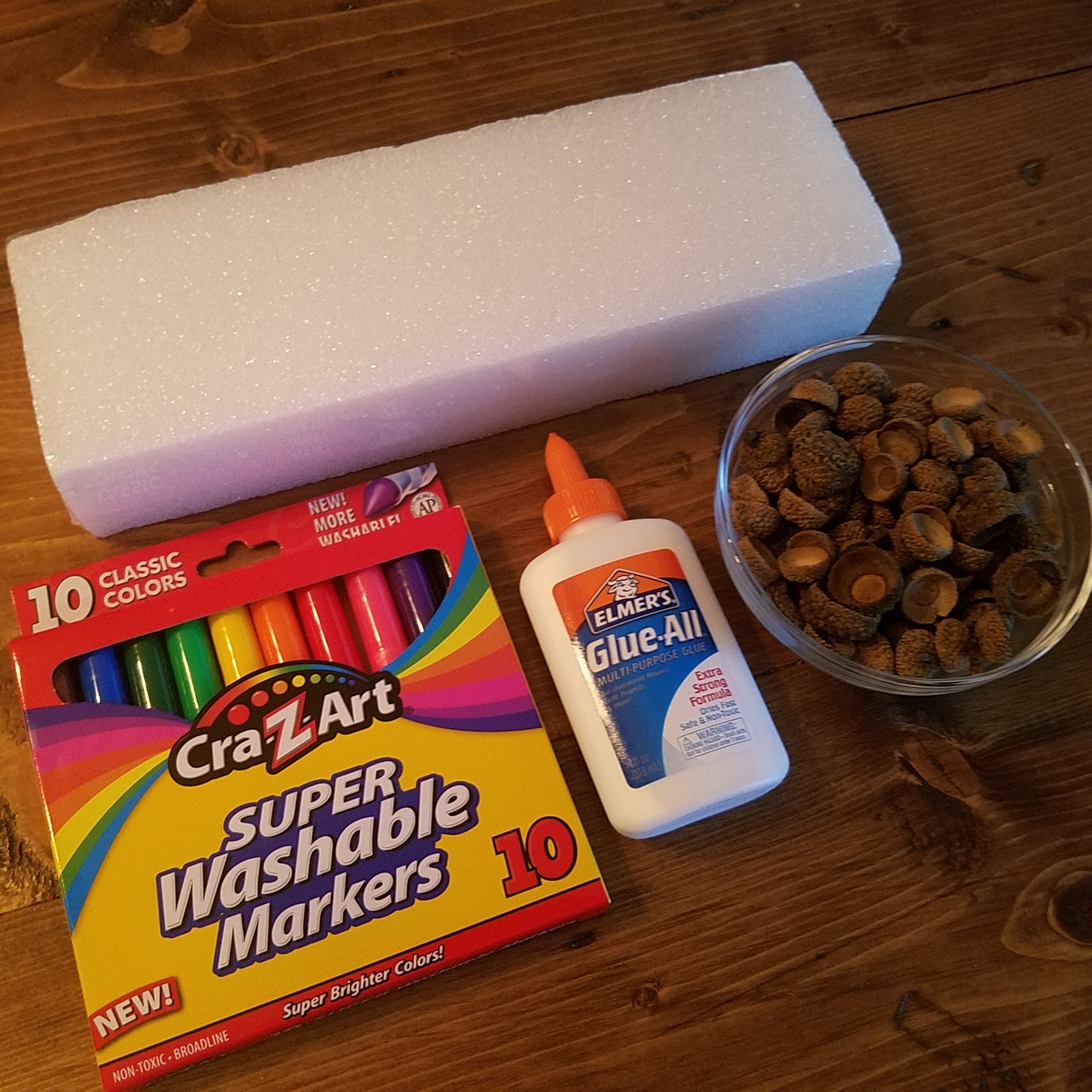 Ingredients to make acorn gems: markers, school glue, acorn caps, and styrofoam